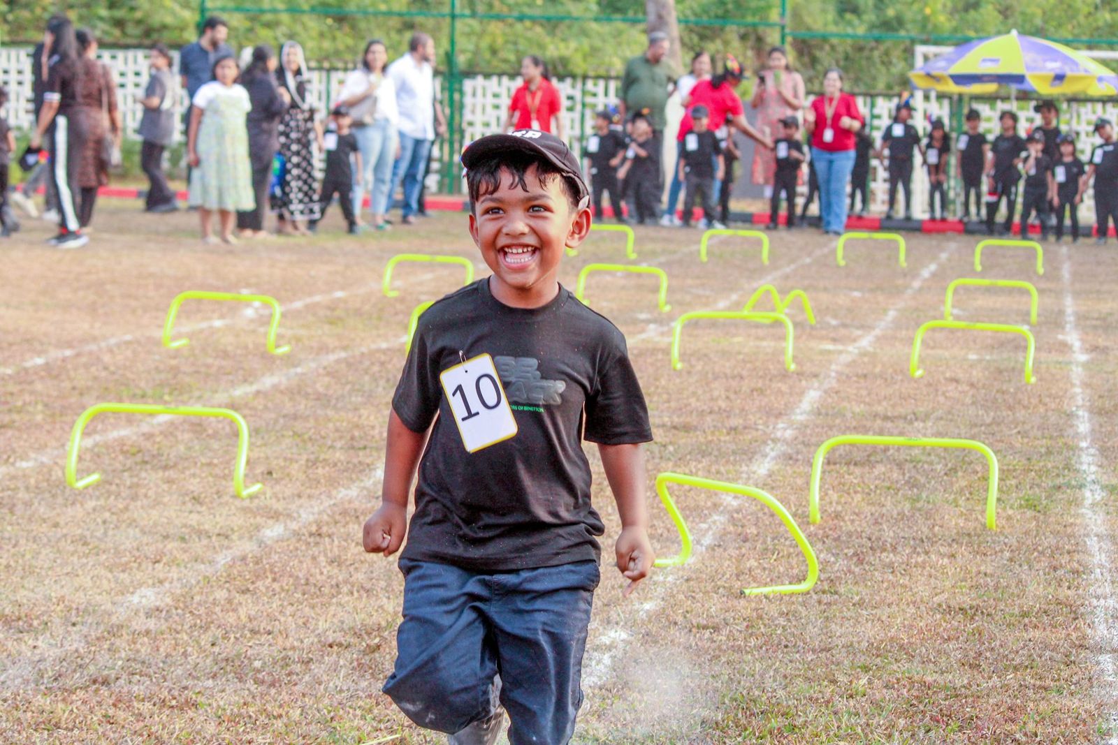 A child mid-race, grinning, at a GEMS athletics meet.