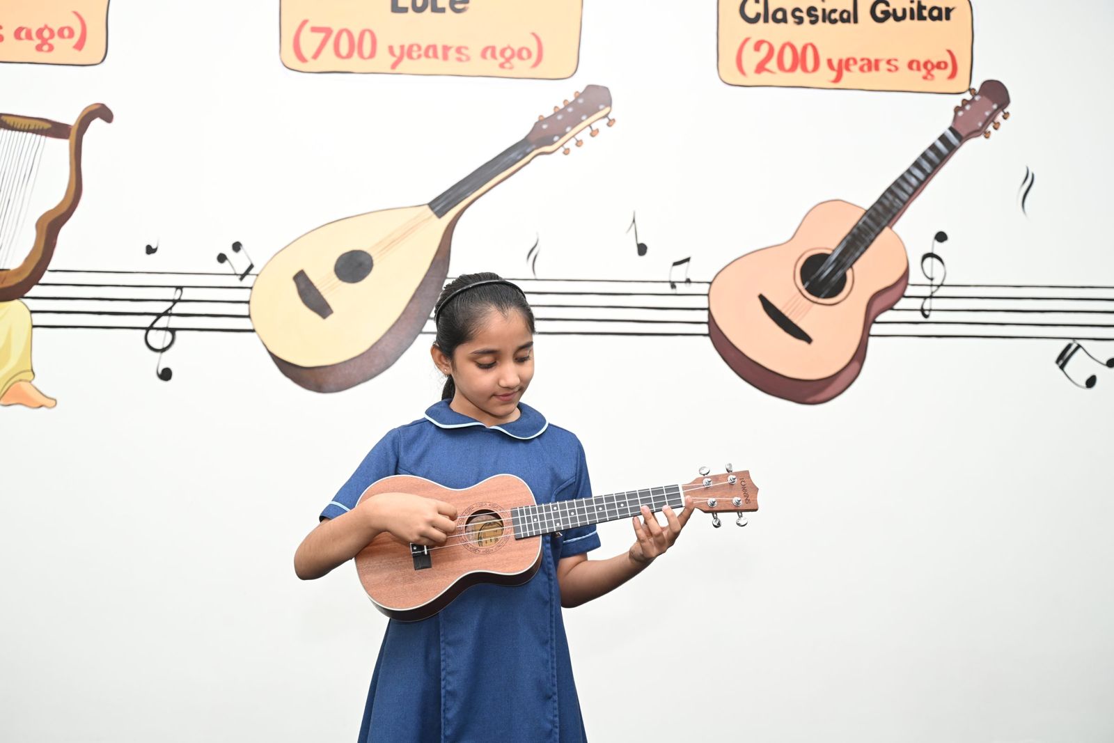 A child playing a stringed instrument in front of a music mural.