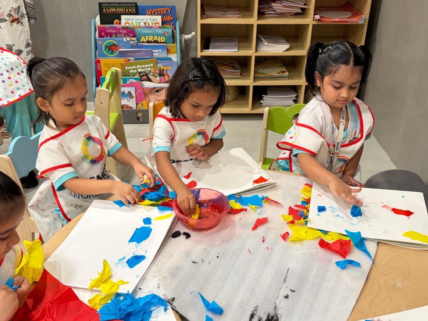 Children dipping pieces of red, blue and yellow kite paper in water before pressing them onto paper