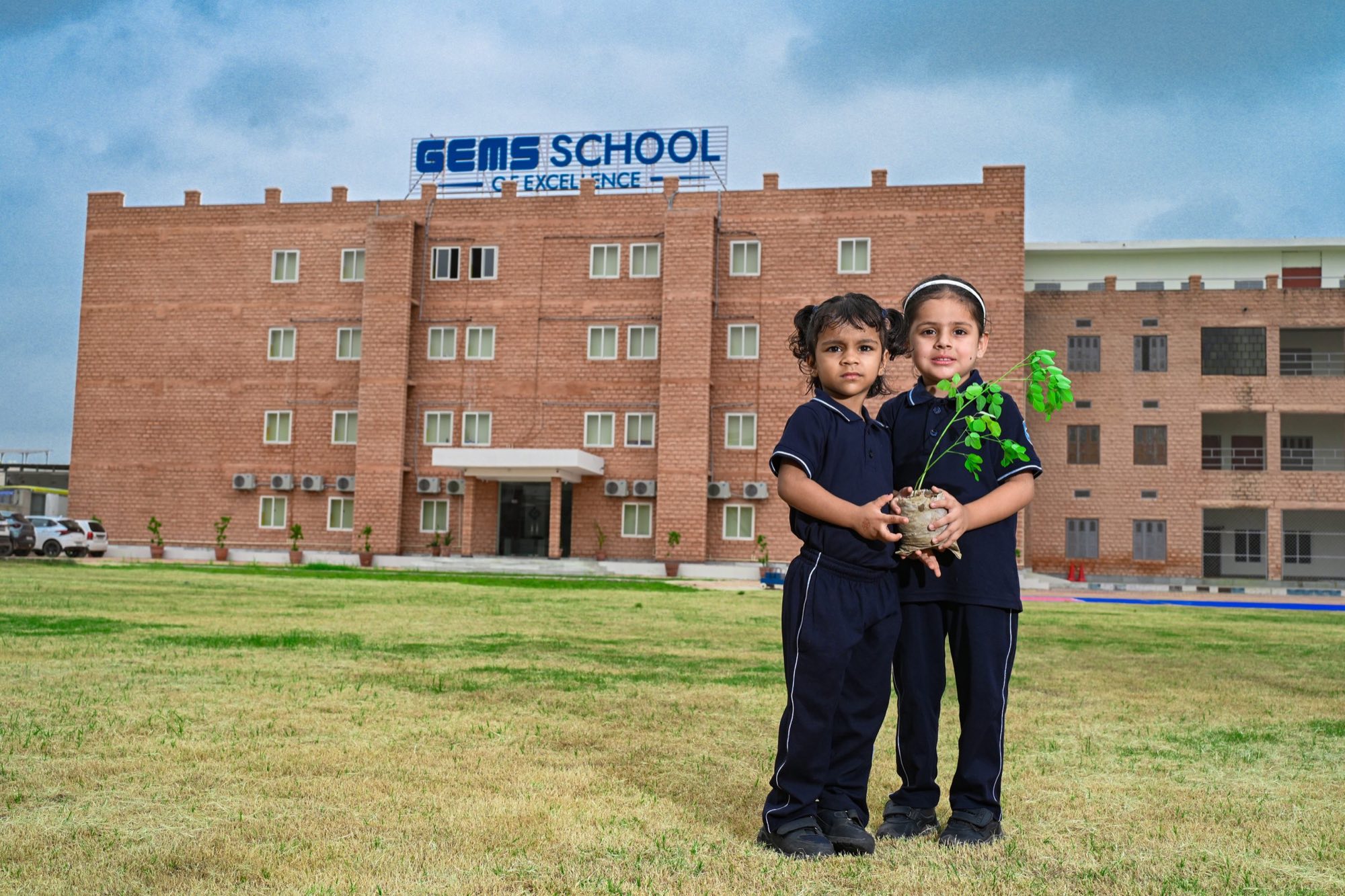 Two young students holding a plant in front of the school building