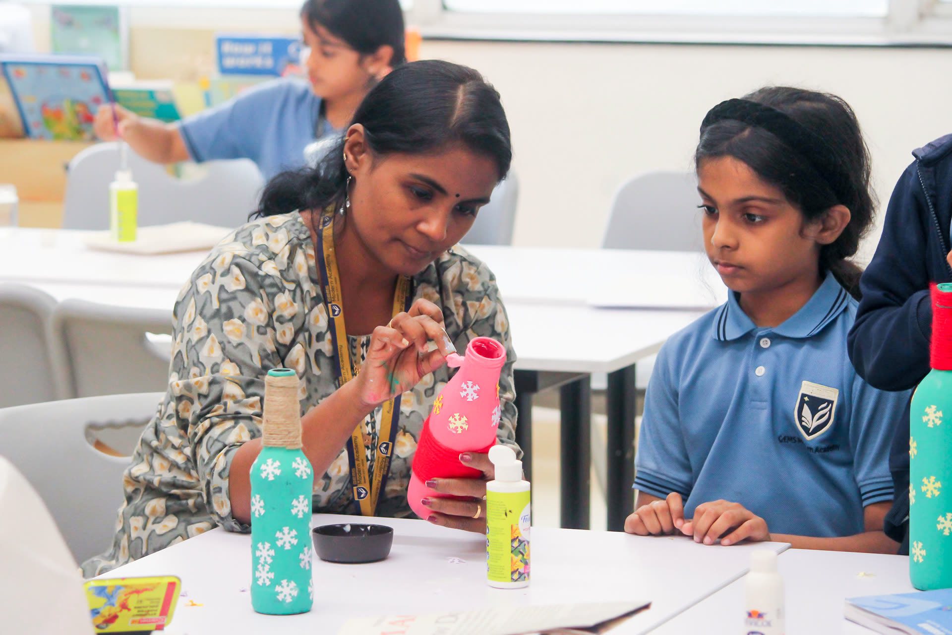 A teacher and a student decorating bottles in an art activity